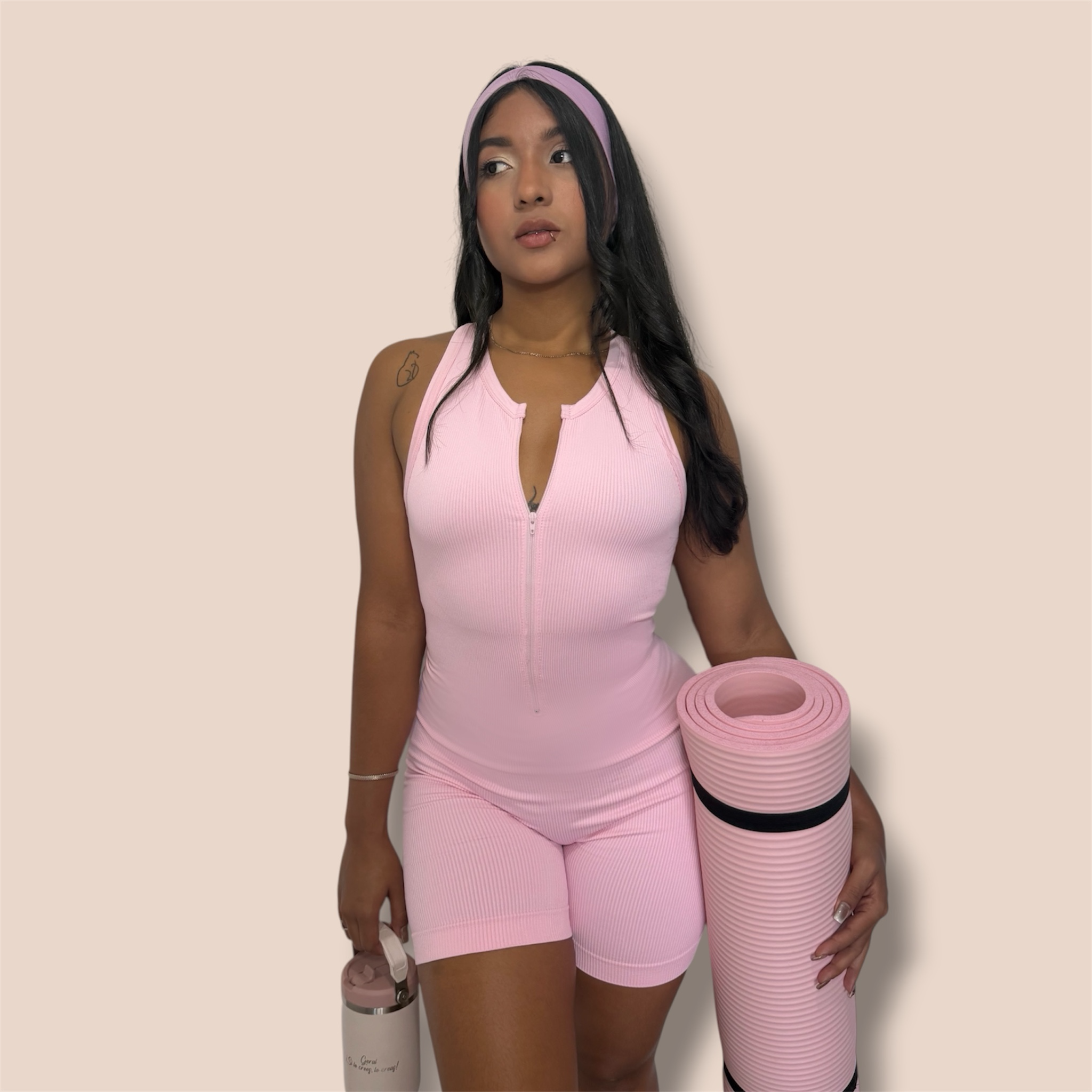 CASH SPORTWEAR light pink ribbed zipper romper bodysuit with racerback, worn by a model holding a yoga mat.